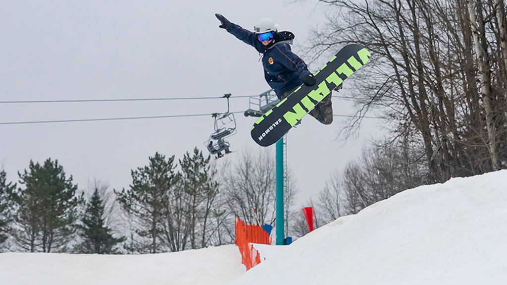 A snowboarder hits a hip jump and grabs his board.
